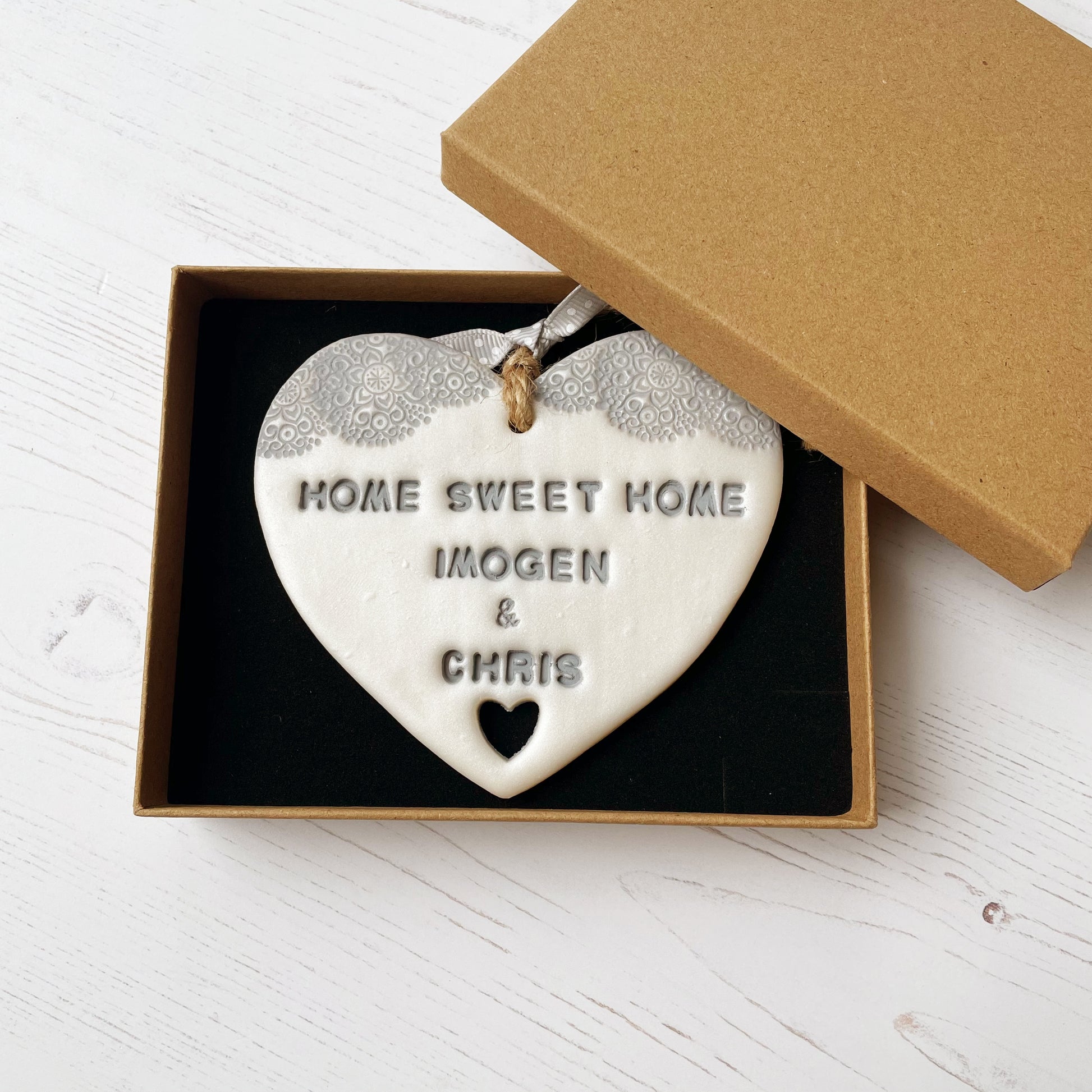 Personalised new home gift pearlised white clay heart with a grey lace edge at the top & a heart cut out at the bottom with twine for hanging personalised with HOME SWEET HOME IMOGEN & CHRIS