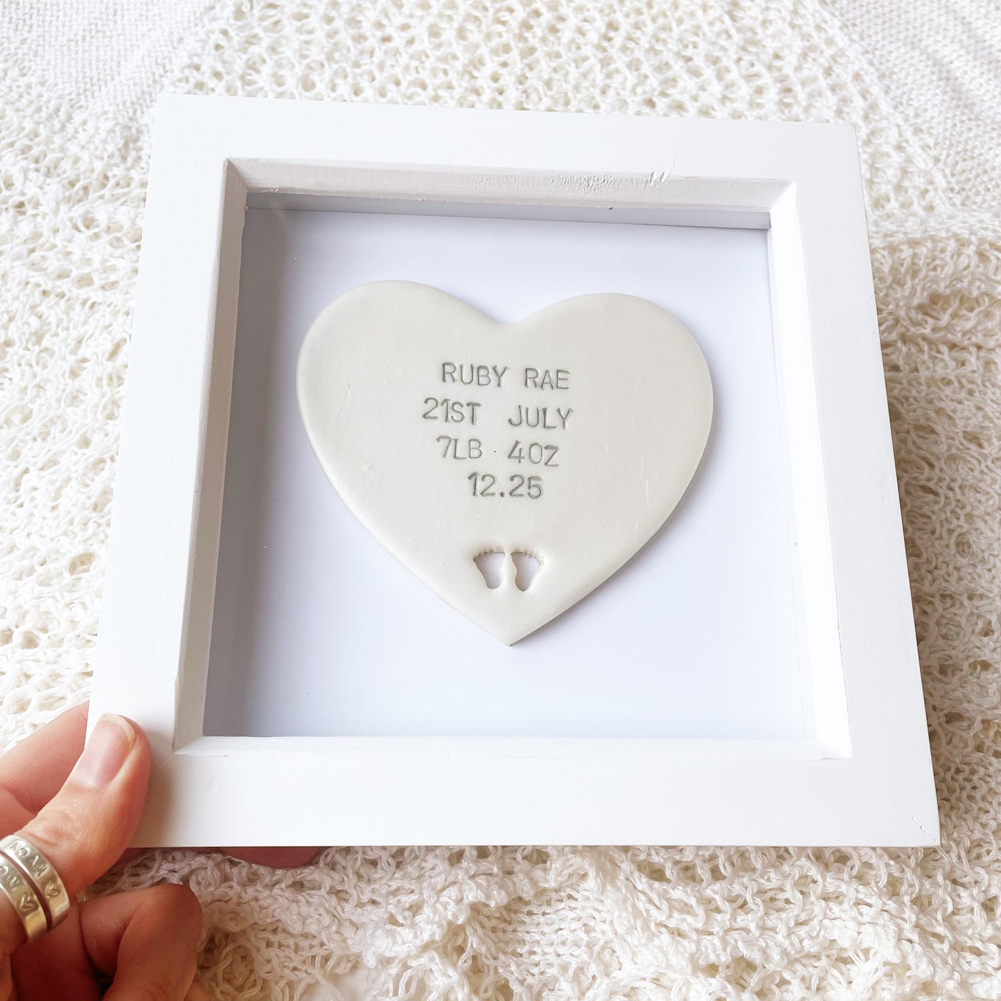 Personalised baby keepsake gift, pearlised white clay heart with baby feet cut out at the bottom of the heart and grey personalisation in a white box frame, the heart is personalised with the baby’s name, date of birth, weight and time