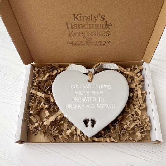 Grey clay hanging heart with baby feet cut out of the bottom and white personalisation, the heart is personalised with CONGRATULATIONS YOU’VE BEEN PROMOTED TO GRANNY AND POPPA!!