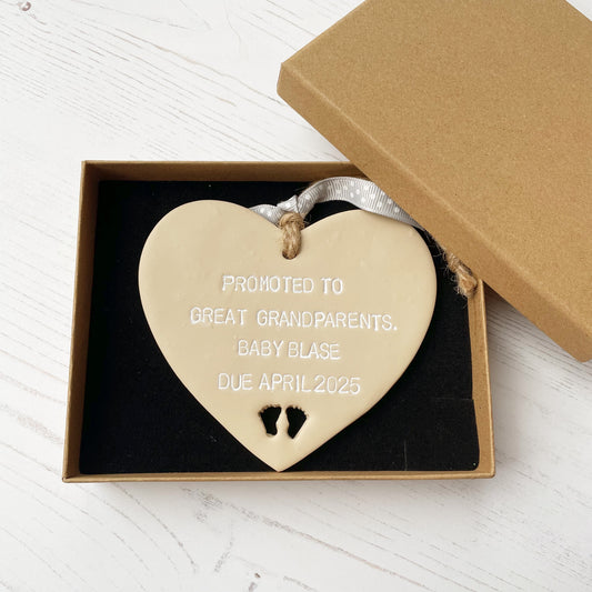 Beige clay hanging heart with baby feet cut out of the bottom and white personalisation, the heart is personalised with PROMOTED TO GREAT GRANDPARENTS. BABY BLASE DUE APRIL 2025