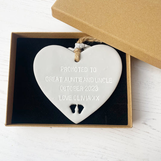 Grey clay hanging heart with baby feet cut out of the bottom and white personalisation, the heart is personalised with PROMOTED TO GREAT AUNTIE AND UNCLE OCTOBER 2023 LOVE OLIVIA XX