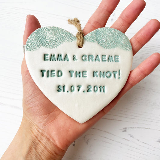 Personalised wedding gift, pearlised white clay hanging heart with a sage green lace edge at the top of the heart, the heart is personalised with EMMA & GRAEME TIED THE KNOT! 31.07.2011