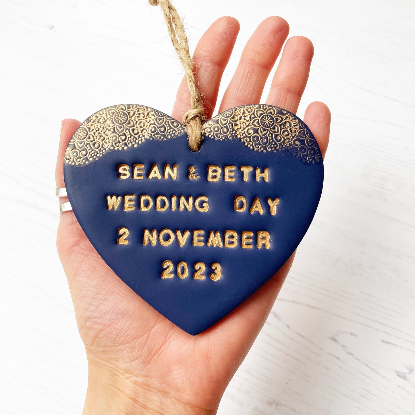 Personalised wedding gift, navy clay heart with a gold lace edge at the top of the heart with twine to hang, the heart is personalised with SEAN & BETH WEDDING DAY 2 NOVEMBER 2023