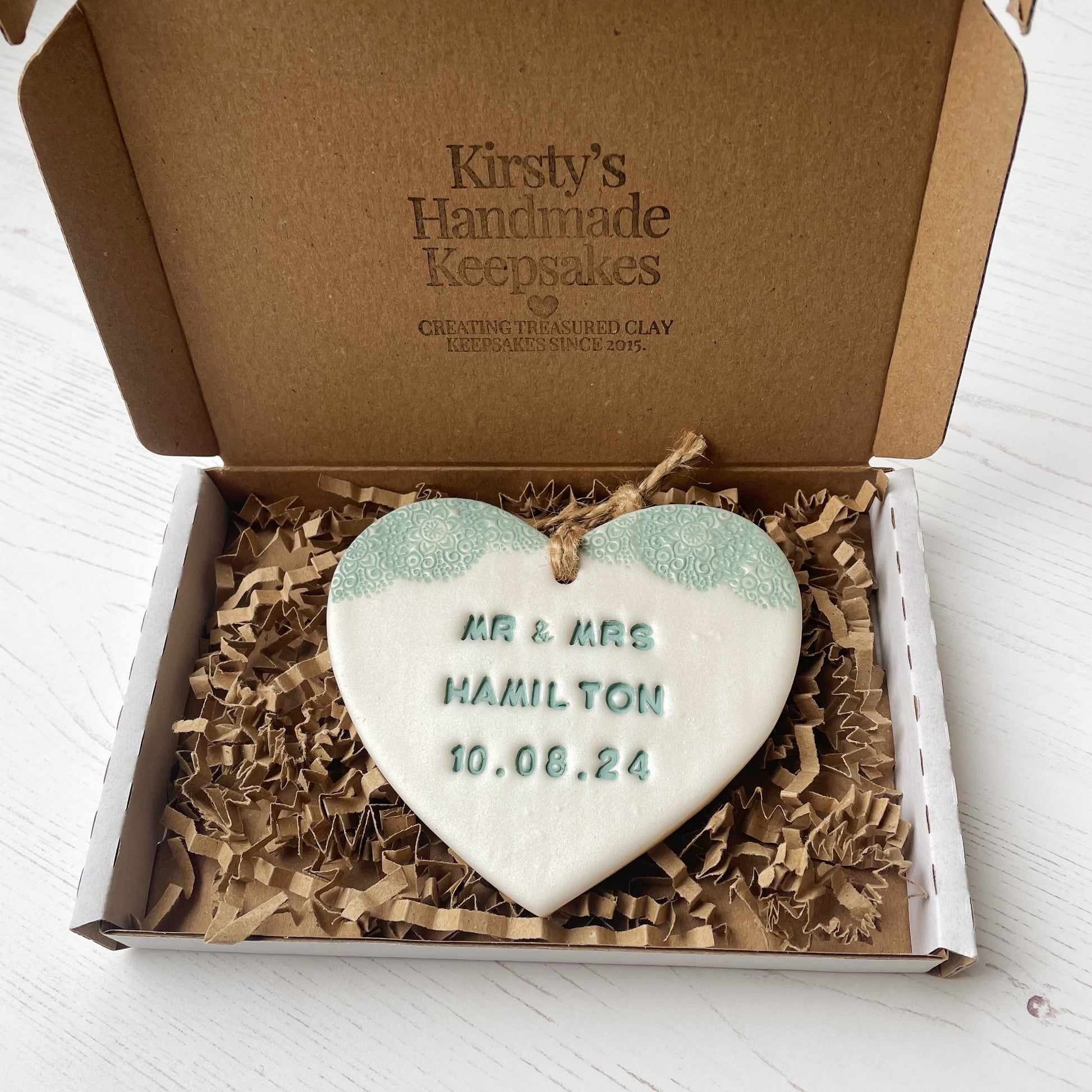 Personalised wedding gift, pearlised white clay hanging heart with a sage green lace edge at the top of the heart, the heart is personalised with MR & MRS HAMILTON 10.08.24