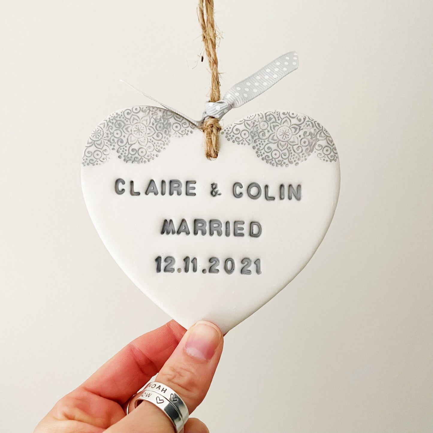 Personalised wedding gift, pearlised white clay hanging heart with a grey lace edge at the top of the heart, the heart is personalised with CLAIRE & COLIN MARRIED 12.11.2021