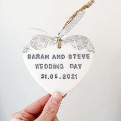 Personalised wedding day gift, pearlised white clay hanging heart with a grey lace edge at the top of the heart, the heart is personalised with SARAH AND STEVE WEDDING DAY 31.05.2021