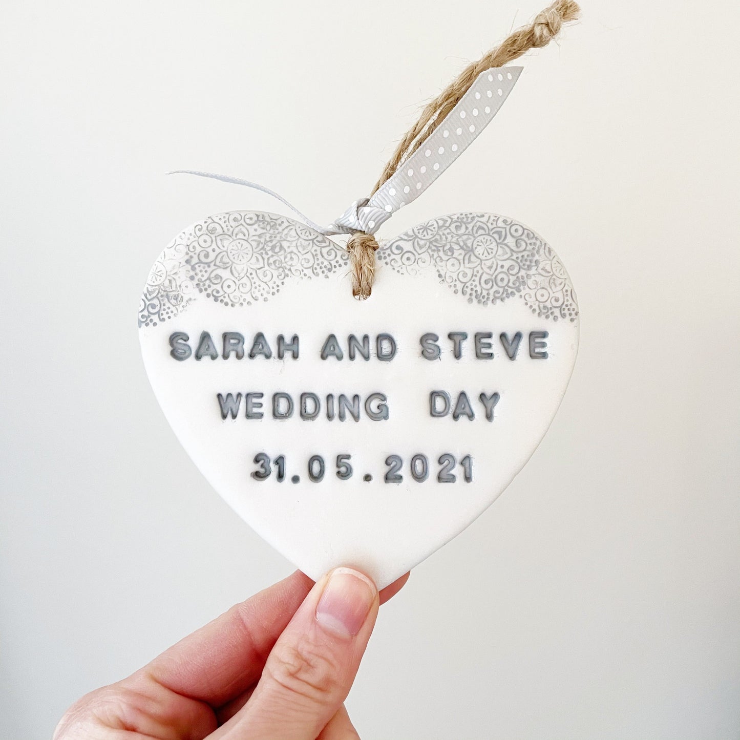 Personalised wedding day gift, pearlised white clay hanging heart with a grey lace edge at the top of the heart, the heart is personalised with SARAH AND STEVE WEDDING DAY 31.05.2021