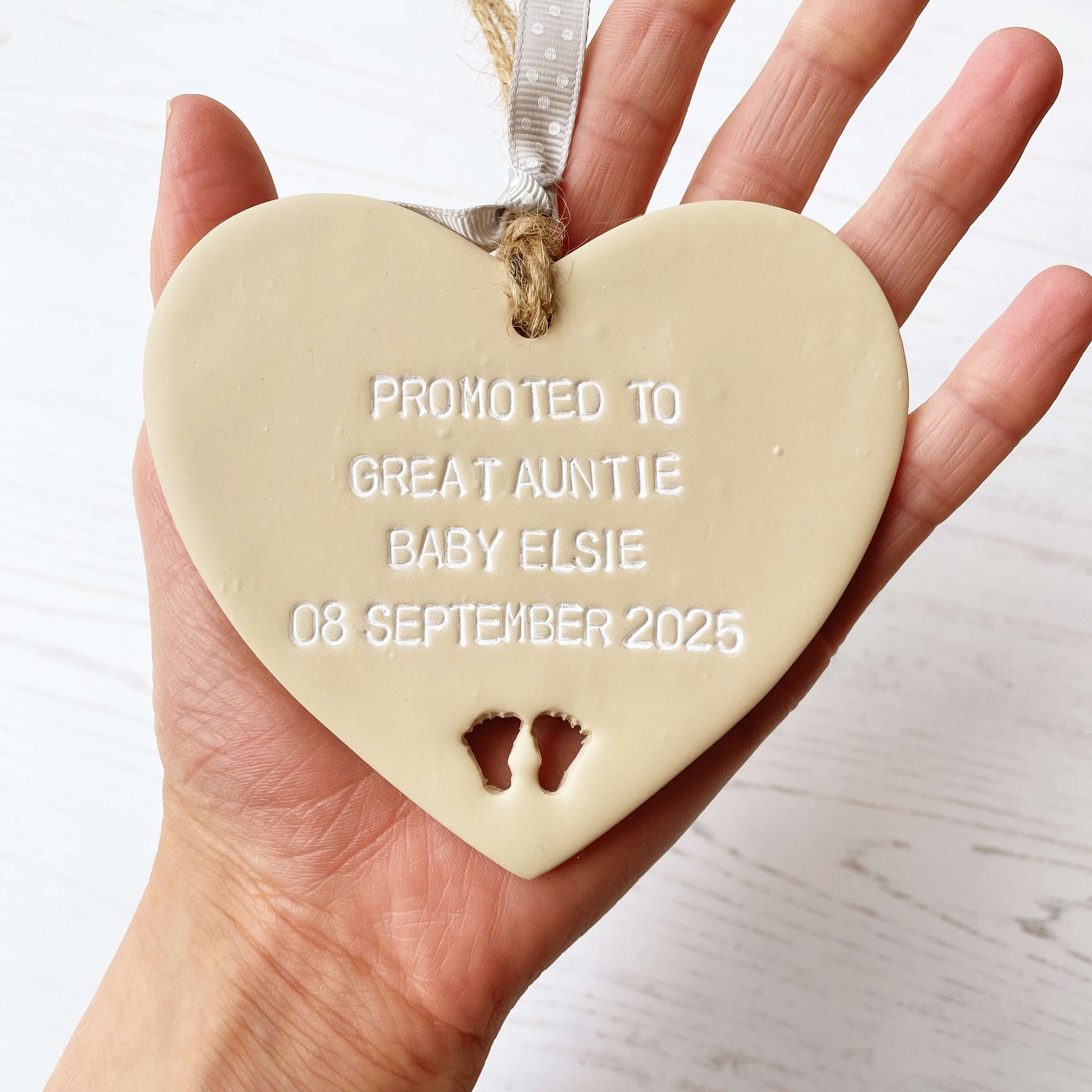 Beige clay hanging heart with baby feet cut out of the bottom and white personalisation, the heart is personalised with PROMOTED TO GREAT AUNTIE BABY ELSIE 08 SEPTEMBER 2025
