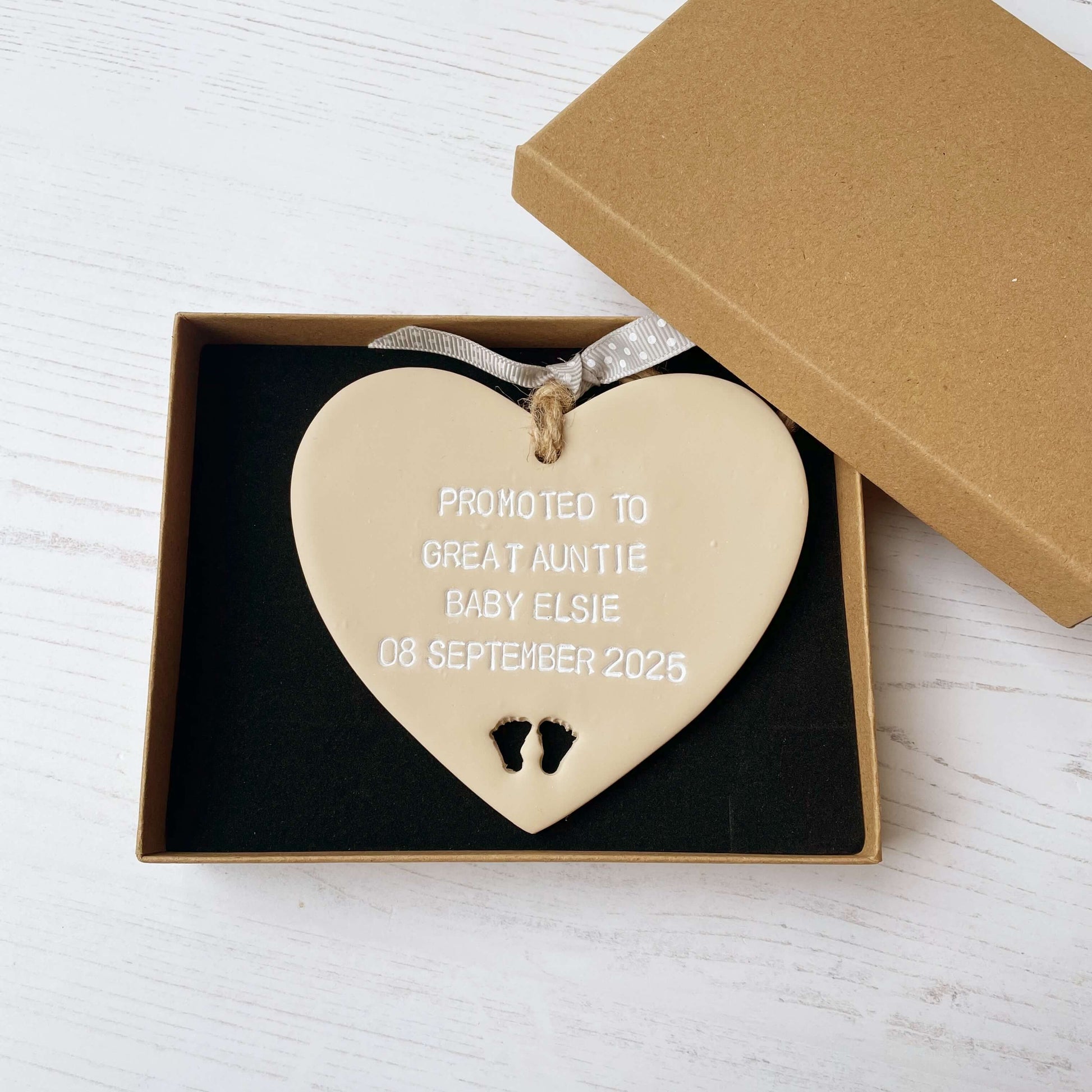 Beige clay hanging heart with baby feet cut out of the bottom and white personalisation, the heart is personalised with PROMOTED TO GREAT AUNTIE BABY ELSIE 08 SEPTEMBER 2025