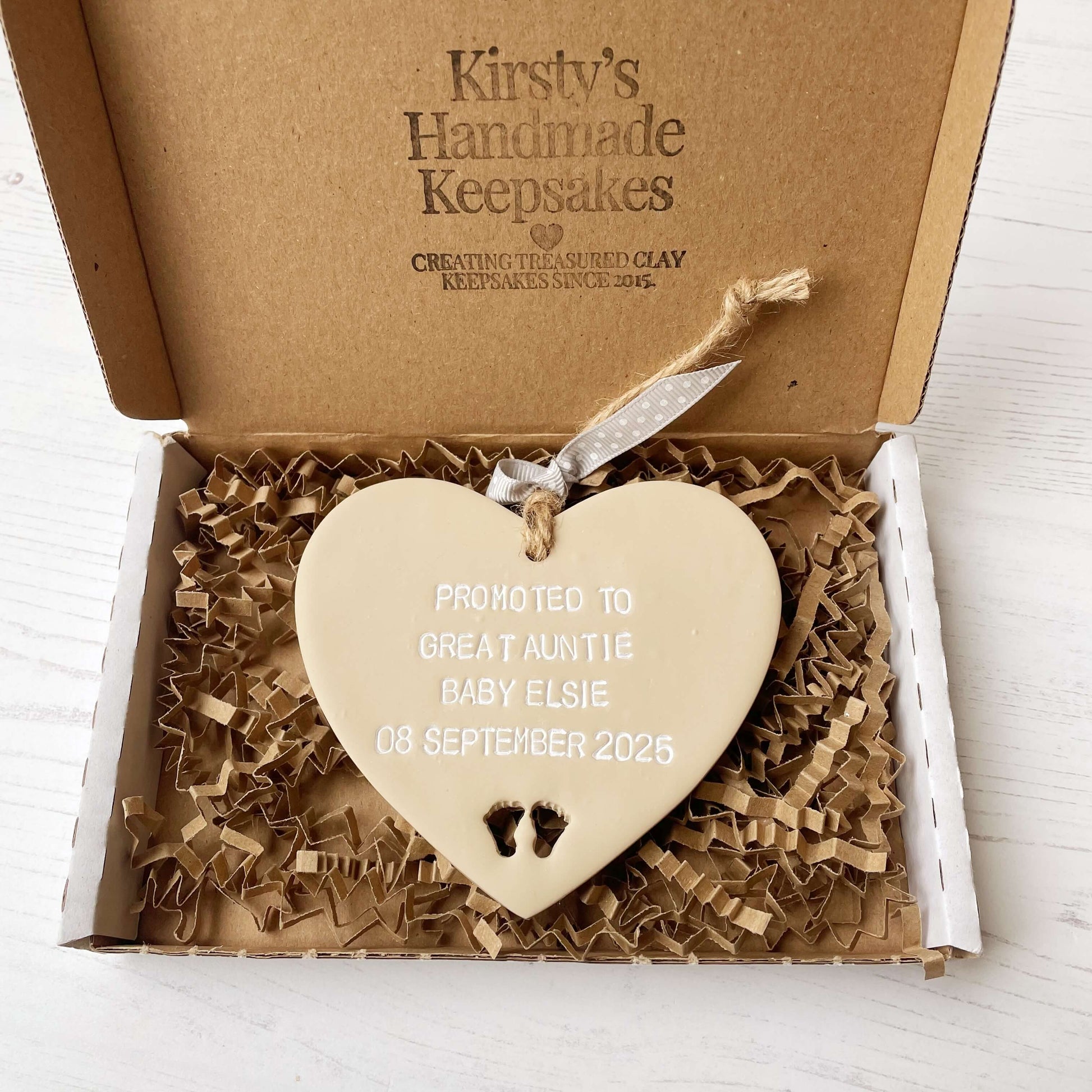 Beige clay hanging heart with baby feet cut out of the bottom and white personalisation, the heart is personalised with PROMOTED TO GREAT AUNTIE BABY ELSIE 08 SEPTEMBER 2025