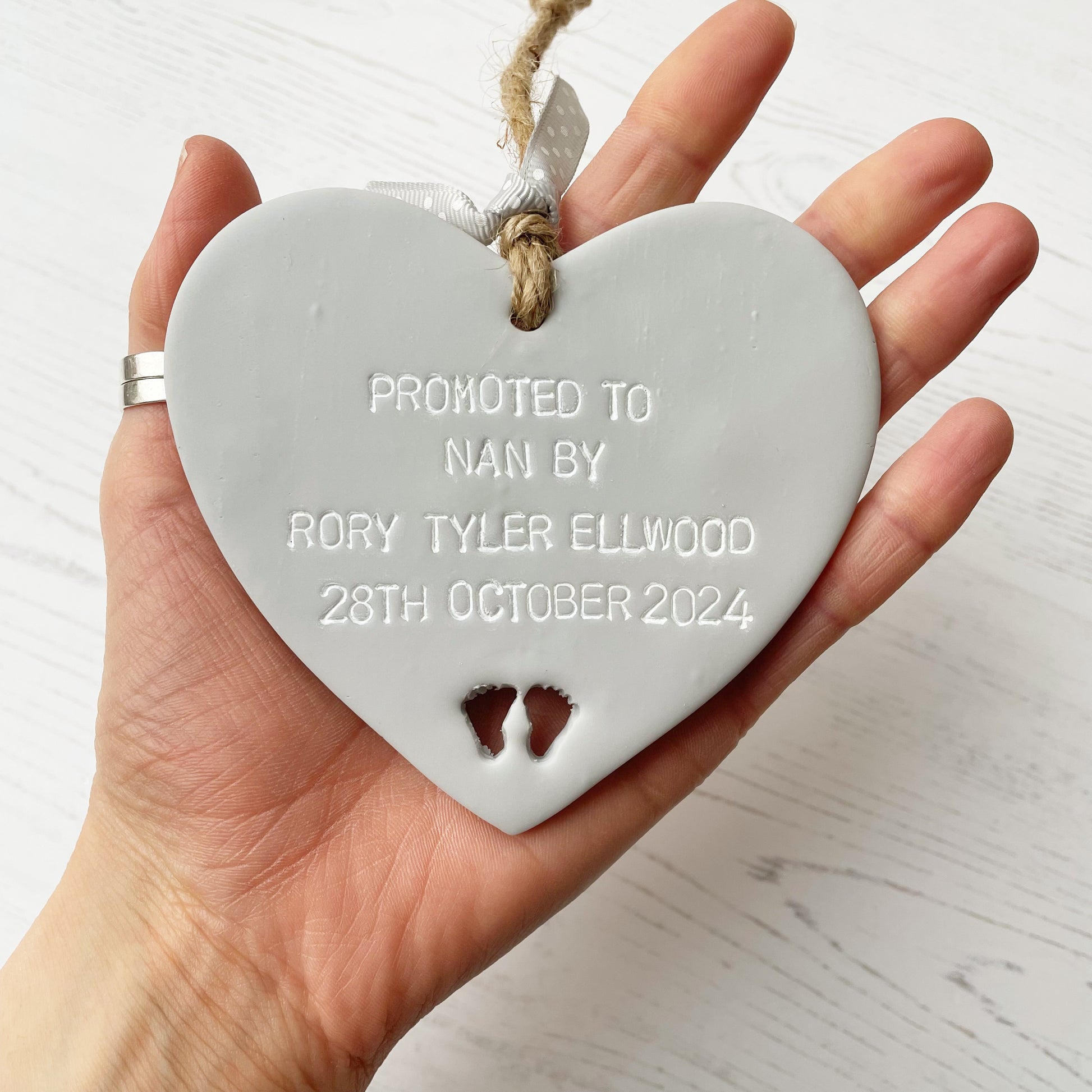 Grey clay hanging heart with baby feet cut out of the bottom and white personalisation, the heart is personalised with PROMOTED TO NAN BY RORY TYLER ELLWOOD 28TH OCTOBER 2024