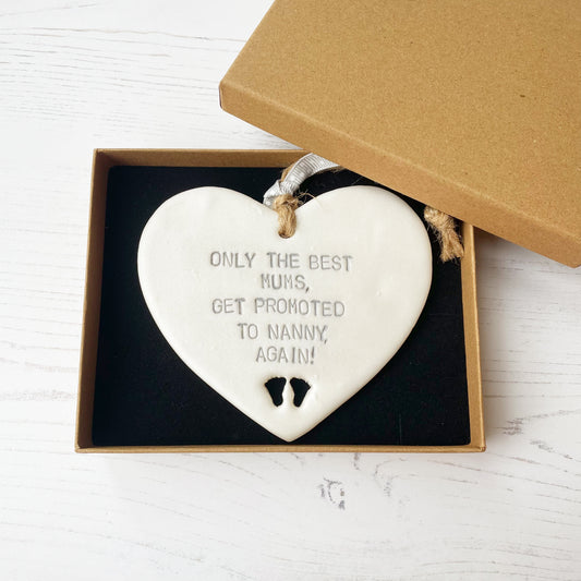 Pearlised white clay hanging heart with baby feet cut out of the bottom and grey personalisation, the heart is personalised with ONLY THE BEST MUMS, GET PROMOTED TO NANNY, AGAIN!