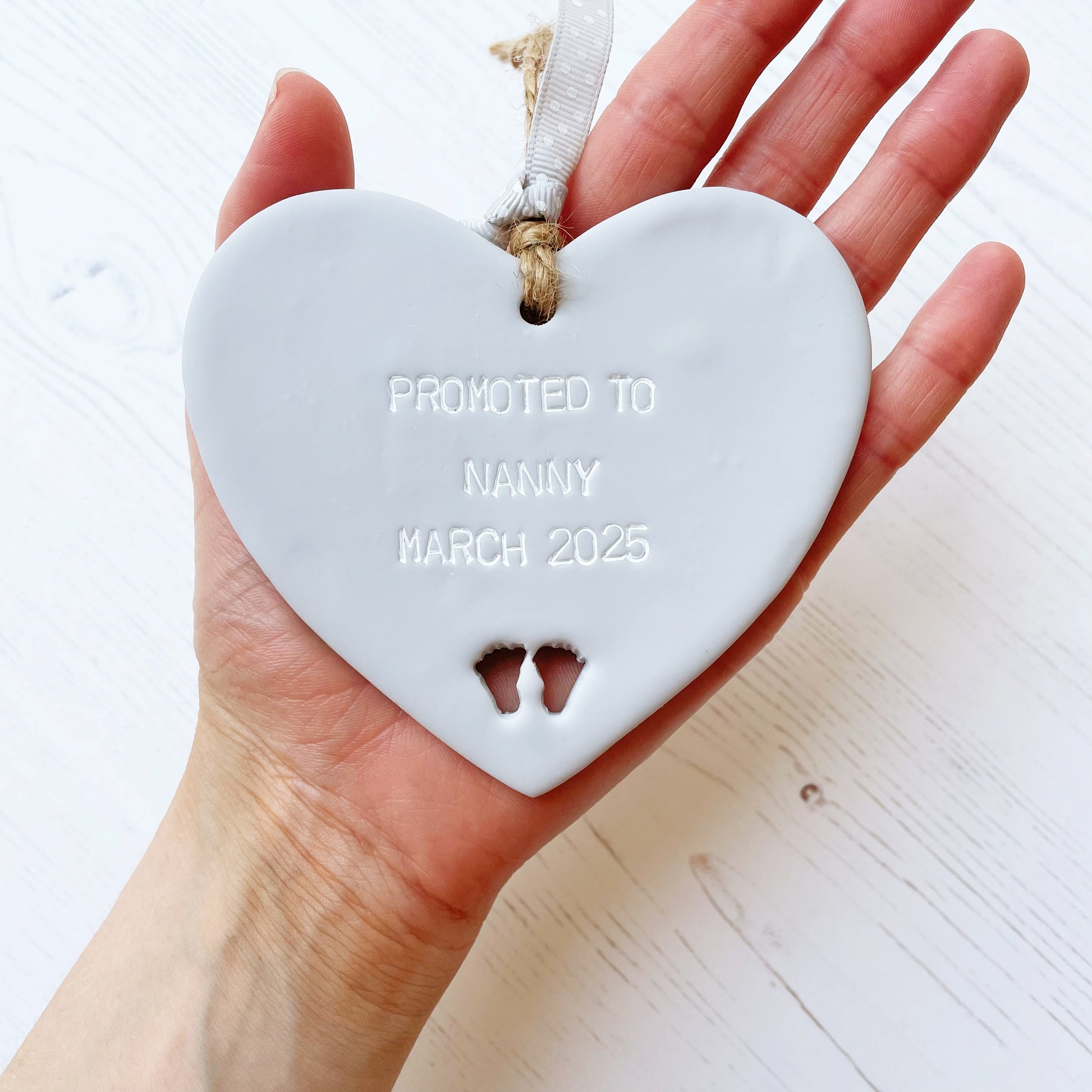 Promoted to Grandparents Grey clay hanging heart with baby feet cut out of the bottom and white personalisation, the heart is personalised with PROMOTED TO NANNY MARCH 2025