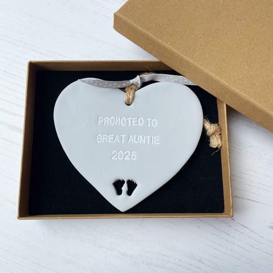 Grey clay hanging heart with baby feet cut out of the bottom and white personalisation, the heart is personalised with PROMOTED TO GREAT AUNTIE 2025