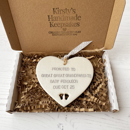 Pearlised white clay hanging heart with baby feet cut out of the bottom and grey personalisation, the heart is personalised with PROMOTED TO GREAT GREAT GRANDPARENTS BABY FERGUSON DUE OCT 2025