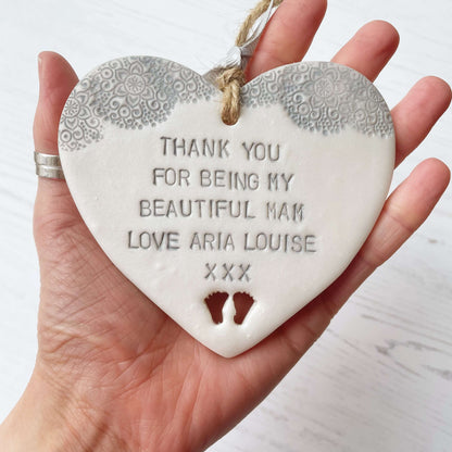 Personalised Mother’s Day gift, pearlised white clay hanging heart with baby feet cut out at the bottom of the heart and a grey lace edge at the top of the heart, the heart is personalised with THANK YOU FOR BEING MY BEAUTIFUL MAM LOVE ARIA LOUISE XXX