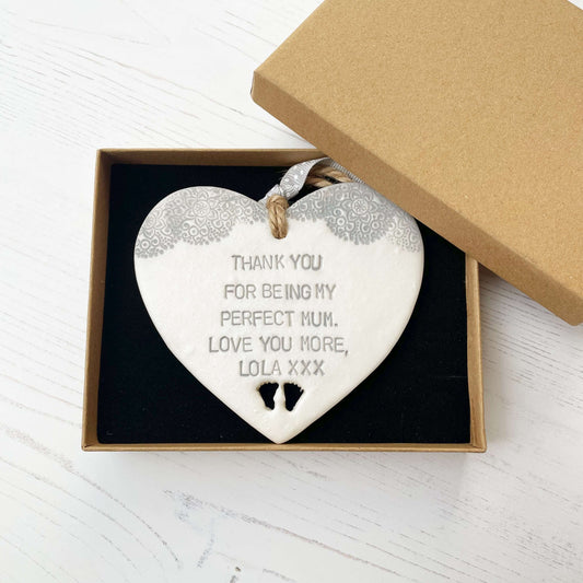 Personalised Mother’s Day gift, pearlised white clay hanging heart with baby feet cut out at the bottom of the heart and a grey lace edge at the top of the heart, the heart is personalised with THANK YOU FOR BEING MY PERFECT MUM. LOVE YOU MORE, LOLA XXX