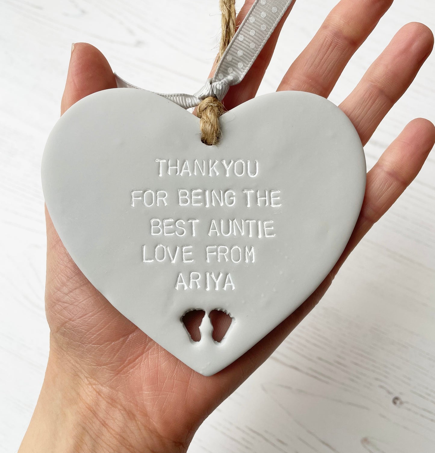 Grey clay hanging heart with baby feet cut out of the bottom and white personalisation, the heart is personalised with THANKYOU FOR BEING THE BEST AUNTIE LOVE FROM ARIYA