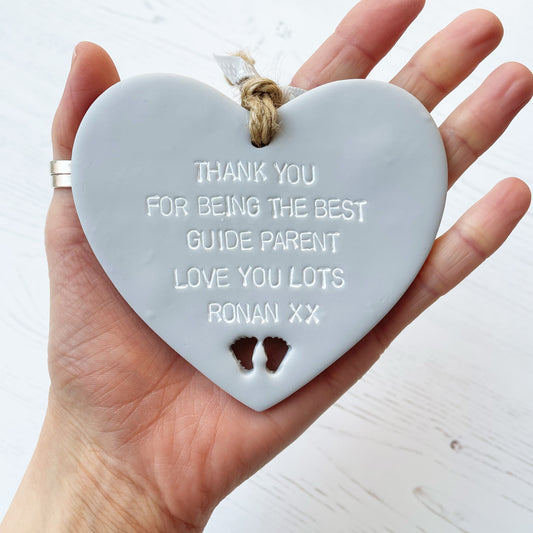 Personalised guide parents gift, grey clay hanging heart with baby feet cut out of the bottom, the heart is personalised in white with THANK YOU FOR BEING THE BEST GUIDE PARENT LOVE YOU LOTS RONAN XX