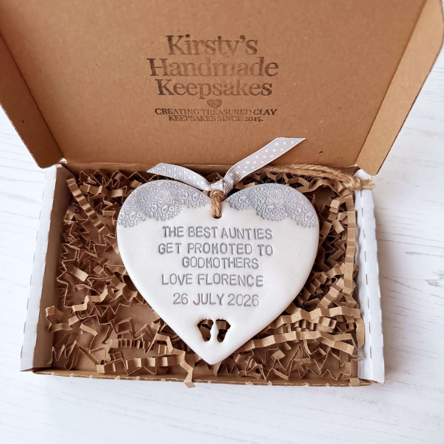 Personalised Godmother gift, pearlised white clay hanging heart with baby feet cut out of the bottom and grey lace edge at the top of the heart, the heart is personalised with THE BEST AUNTIES GET PROMOTED TO GODMOTHERS LOVE FLORENCE 26 JULY 2026