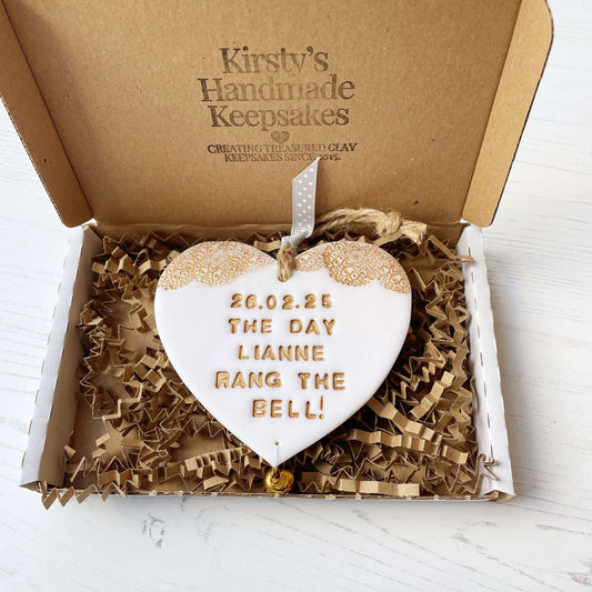 Personalised cancer survivor gift, glitter white clay hanging heart with a gold lace edge at the top of the heart and a gold bell hanging below, the heart is personalised with 26.02.25 THE DAY LIANNE RANG THE BELL!