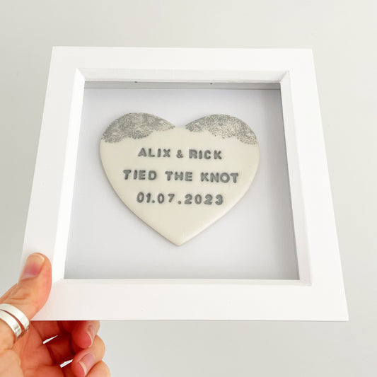 Personalised framed wedding heart gift, pearlised white clay heart with a grey lace edge at the top of the heart in a white box frame, the heart is personalised with ALIX & RICK TIED THE KNOT 01.07.2023