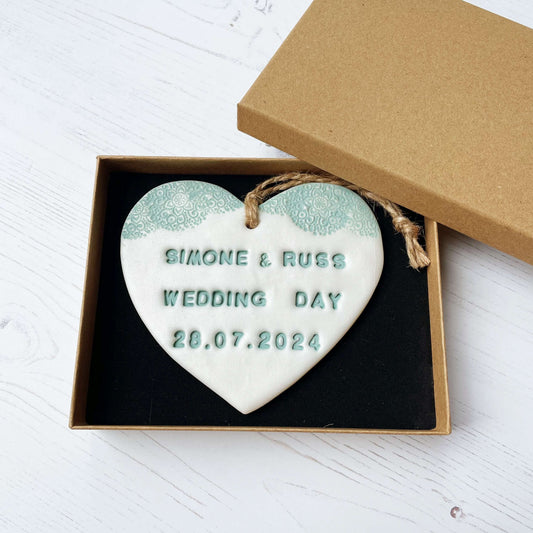 Personalised wedding gift, pearlised white clay heart with a sage green lace edge at the top of the heart with twine to hang, the heart is personalised with SIMONE & RUSS WEDDING DAY 28.07.2024