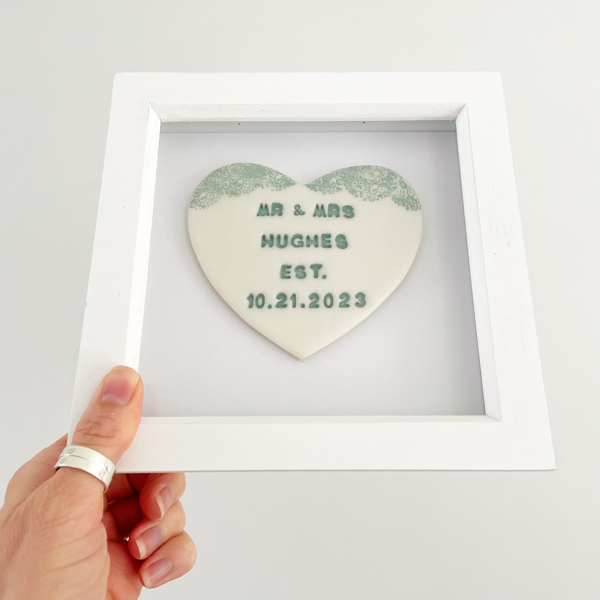 Personalised framed wedding heart gift, pearlised white clay heart with a sage green lace edge at the top of the heart in a white box frame, the heart is personalised with MR & MRS HUGHES EST. 10.21.2023