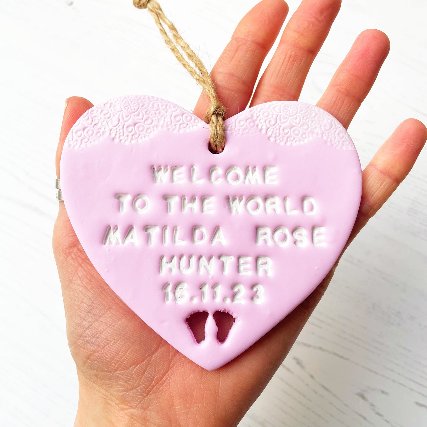 Personalised baby announcement heart sign, in pink clay hanging heart with a white writing and baby feet cut out at the bottom of the heart, the heart is personalised with WELCOME TO THE WORLD BABY MATILDA ROSE HUNTER 16.11.23
