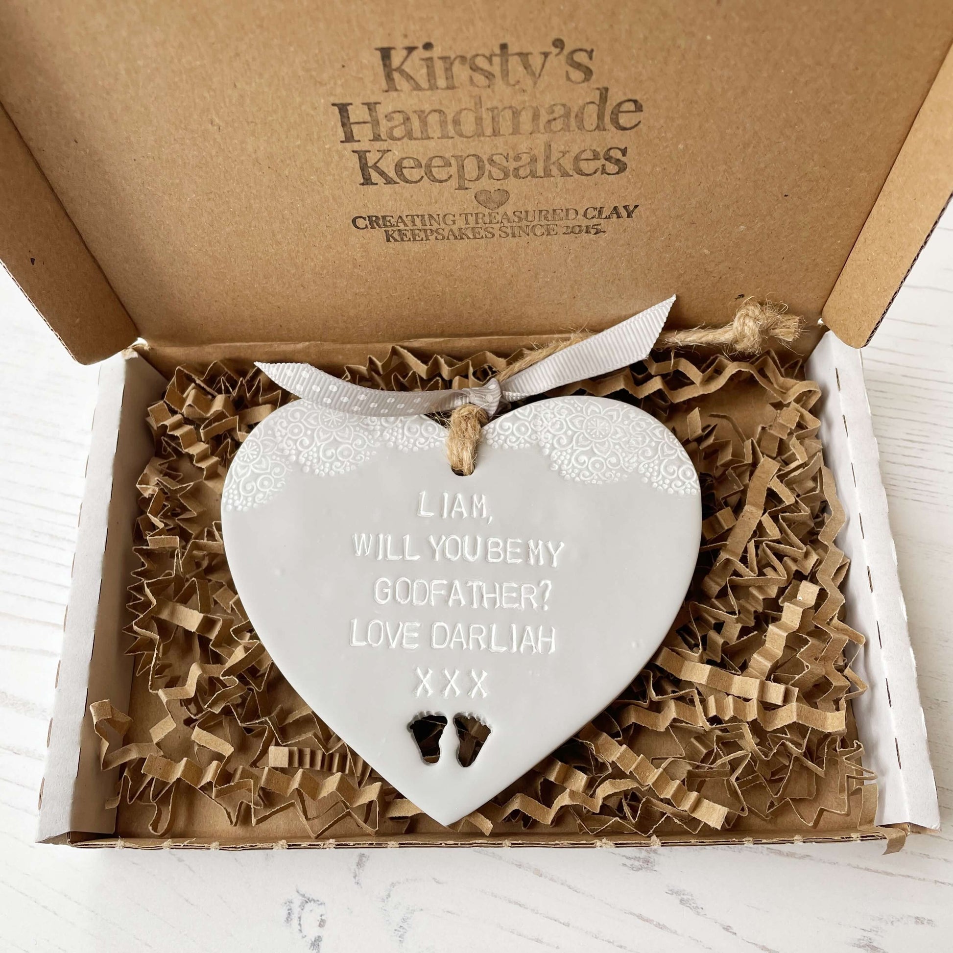 Personalised Godfather proposal gift, grey clay hanging heart with baby feet cut out of the bottom and white lace edge at the top of the heart, the heart is personalised with LIAM, WILL YOU BE MY GODFATHER? LOVE DARLIAH XXX