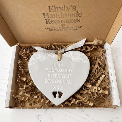 Personalised Godfather proposal gift, grey clay hanging heart with baby feet cut out of the bottom and white lace edge at the top of the heart, the heart is personalised with LIAM, WILL YOU BE MY GODFATHER? LOVE DARLIAH XXX