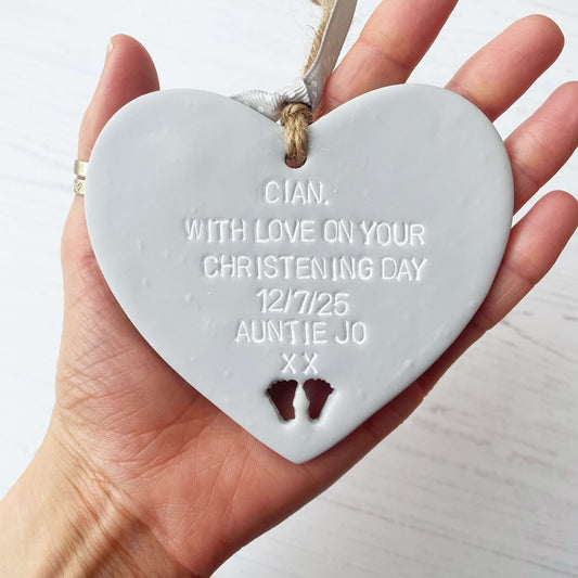 Personalised Christening baptism gift, grey clay hanging heart, with baby feet cut out of the bottom, the heart is personalised with CIAN, WITH LOVE ON YOUR CHRISTENING DAY 12/7/25 AUNTIE JO XX