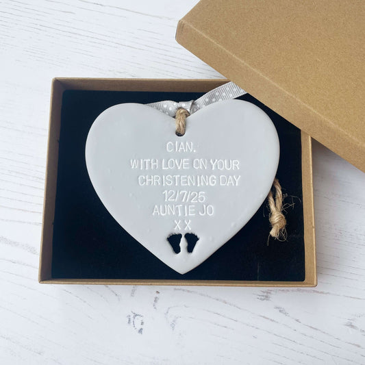 Personalised Christening baptism gift, grey clay hanging heart, with baby feet cut out of the bottom, the heart is personalised with CIAN, WITH LOVE ON YOUR CHRISTENING DAY 12/7/25 AUNTIE JO XX
