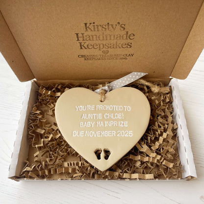 Beige clay hanging heart with baby feet cut out of the bottom and white personalisation, the heart is personalised with YOU’RE PROMOTED TO AUNTIE CHLOE! BABY MAINPRIZE DUE NOVEMBER 2025