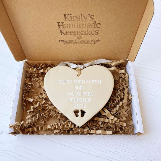 Beige clay hanging heart with baby feet cut out of the bottom and white personalisation, the heart is personalised with YOU’RE SUCH A GREAT MUM, YOU’VE BEEN PROMOTED 2025